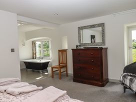 A bedroom with a wooden chest of drawers a wooden chair and a freestanding bathtub by a window at Puddaven Barn in North Bovey near Chagford