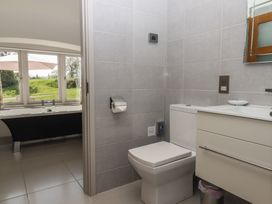 A bathroom with a toilet and sink and a bathtub by windows showing an outside view at Puddaven Barn in North Bovey near Chagford
