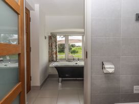 A bathroom with a bathtub under a window and a toilet paper holder on a tiled wall at Puddaven Barn North Bovey near Chagford