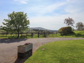 A rural scene with a grassy area a tree a flower planter a fenced field and hills in the background at Puddaven Barn in North Bovey near Chagford