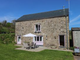 A stone house with pink doors and windows and outdoor table with umbrella on gravel at Puddaven Barn North Bovey near Chagford