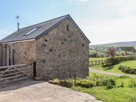 A stone barn with a wooden gate and a garden beside a driveway in a countryside setting at Puddaven Barn in North Bovey near Chagford