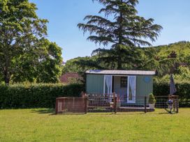 A small garden shed with open doors and a fenced grassy yard surrounded by trees at Songbirds in St Michaels Kent