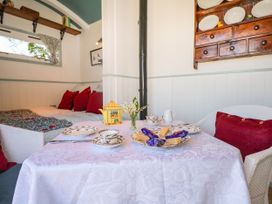 A small dining area with a table set for tea including cups and snacks a cushioned seating area with red pillows and a mounted wooden cabinet with plates in Songbirds St Michaels Kent