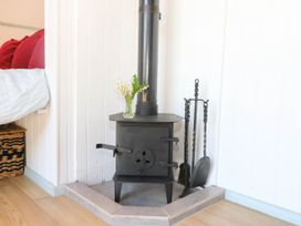 A black metal wood burning stove with a chimney pipe a small vase with flowers on top and fireplace tools next to it in a corner with white paneled walls and wood flooring at Songbirds in St Michaels Kent