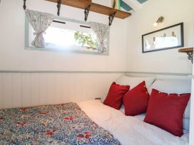 A small bedroom with a bed with red pillows and floral quilt under a window with patterned curtains and a framed bird picture on the wall at Songbirds in St Michaels Kent