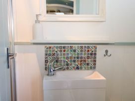 A small bathroom sink with a silver faucet colorful tiled backsplash white soap dispenser and a mirror at Songbirds in St Michaels Kent