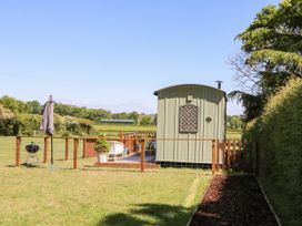 A fenced grassy garden with a small green shed patio chairs umbrella and barbecue in a countryside setting at Songbirds in St Michaels Kent