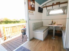 A small dining area with built-in bench seats around a table set with a bottle and glasses inside a room with an open door leading to a wooden deck with a small black metal table and chairs at Songbirds in St Michaels Kent