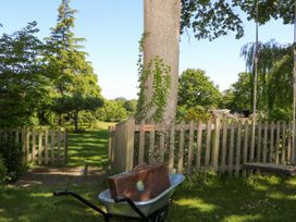 A garden with a wheelbarrow holding a suitcase near a wooden fence and a tree with a swing at Songbirds in St Michaels Kent