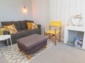 A living area with a grey couch with yellow cushions a wooden chair with yellow fabric a grey ottoman and a white small table at Penzance Apartment in Penzance