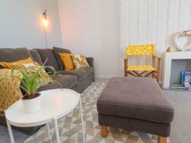 A living room with a grey sofa, yellow cushions, a white round table with a plant, a grey ottoman, and a yellow patterned chair at Penzance Apartment in Penzance