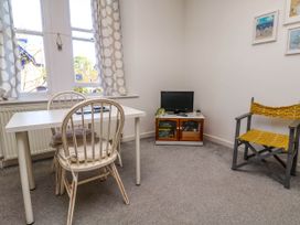 A small room with a white table, two wooden chairs, a small TV on a cabinet, and a yellow fabric chair at Penzance Apartment in Penzance