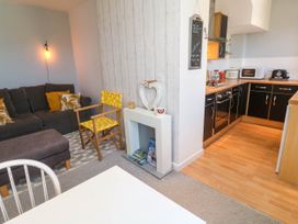 A living room with a gray sofa a yellow chair a small white fireplace and a kitchen with black cabinets at Penzance Apartment in Penzance