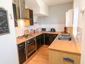 A kitchen with black cabinets wooden countertops gas stove oven microwave toaster and sink at Penzance Apartment in Penzance