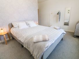 A bedroom with a bed two pillows a bedside table with a lamp a clothes rack with hangers and a mirror on the wall at Penzance Apartment in Penzance