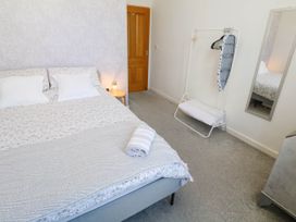 A bedroom with a bed with pillows and a rolled towel a clothes rack with hangers and an ironing board a wall mirror and a wooden door at Penzance Apartment in Penzance