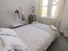 A bedroom with a bed near windows with curtains a small dresser a standing mirror and a clothes rack at Penzance Apartment in Penzance