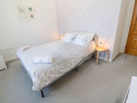 A bedroom with a double bed with pillows and towels a small wooden side table with a lamp and framed pictures on the wall at Penzance Apartment in Penzance