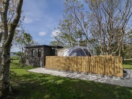 A small building with a transparent geodesic dome and a wooden fence surrounded by trees and grass at Number 2 Dome in Derrybeg County Donegal
