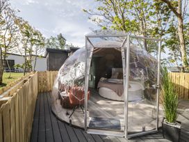 A transparent geodesic dome with a bed and chairs inside on a wooden deck surrounded by a wooden fence at Number 2 Dome in Derrybeg County Donegal