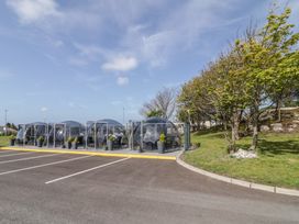 A row of transparent bubble seating pods next to a parking lot with trees and grass at Number 2 Dome in Derrybeg County Donegal