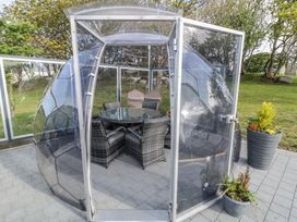 A transparent dome structure with a glass table and chairs inside on a paved patio at Number 2 Dome in Derrybeg County Donegal