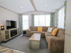 A living room with a brown sectional sofa yellow cushions a wooden coffee table a TV on a stand and floral curtains at HW42 in Bognor Regis