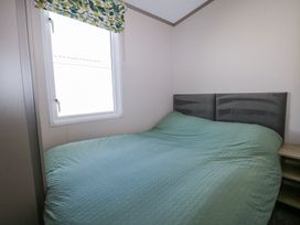 A bedroom with a bed covered by a green textured blanket a small bedside table and a window with green and yellow leaf patterned blinds at HW42 in Bognor Regis