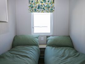 A bedroom with two single beds with green bedding separated by a small wooden nightstand under a window with leaf patterned curtains at HW42 in Bognor Regis