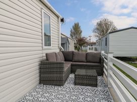 An outdoor patio area with a wicker sofa set and patterned rug beside mobile homes at HW42 in Bognor Regis