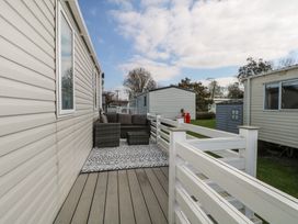 An outdoor deck with a gray sofa set and patterned rug near mobile homes at HW42 in Bognor Regis