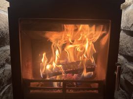A fireplace with flames and burning wood logs at Yew Tree Cottage