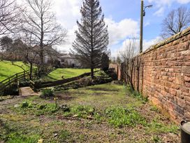 A garden with trees and a wooden bridge at Yew Tree Cottage Mealsgate near Ireby