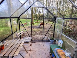 A greenhouse with a table and a dog outside at Yew Tree Cottage Mealsgate near Ireby