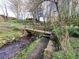 A garden with a wooden bridge over a stream at Yew Tree Cottage Mealsgate near Ireby