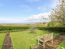 A garden with a wooden bench a small tree and a hedge overlooking a distant landscape at Burry House in Llanmorlais