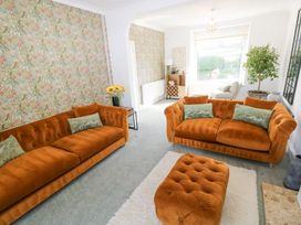 A living room with orange sofas, a matching ottoman, floral wallpaper, a wooden cabinet, and a large window at Burry House Llanmorlais