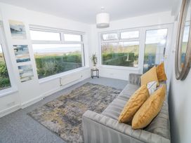 A sitting room with a gray sofa with yellow cushions a patterned rug and large windows showing a garden at Burry House in Llanmorlais