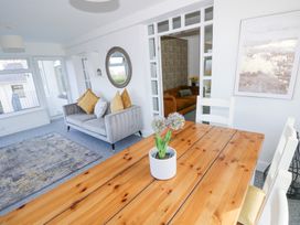 A dining area with a wooden table and white chairs next to a living room with a grey couch and yellow cushions at Burry House in Llanmorlais