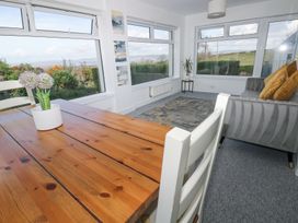 A dining table with a flower pot a grey sofa with cushions a small side table with a plant and large windows with a garden view at Burry House in Llanmorlais