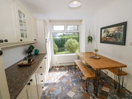 A kitchen dining area with wooden table and benches next to window and cabinets along one wall at Burry House in Llanmorlais