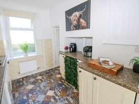 A kitchen with patterned tile floor a window with a plant on the sill appliances and a painting of a highland cow at Burry House in Llanmorlais