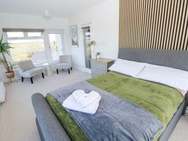 A bedroom with a gray bed and green blanket two armchairs near a window a side table a chest of drawers and a tall plant at Burry House in Llanmorlais