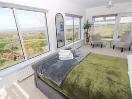 A bedroom with a bed near corner windows and two chairs around a small table at Burry House in Llanmorlais