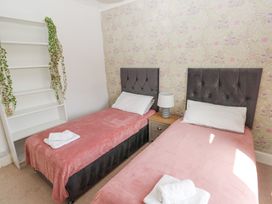 A bedroom with two single beds a nightstand with a lamp and empty shelves with plants at Burry House Llanmorlais