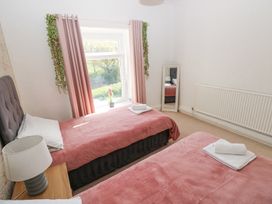 A bedroom with two single beds with pink covers a window with pink curtains a wooden side table with a lamp a standing mirror and a radiator at Burry House in Llanmorlais