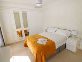 A bedroom with a bed covered with white bedding and a mustard colored blanket two bedside tables with lamps and a large wardrobe with mirrored panels at Burry House in Llanmorlais