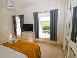 A bedroom with a bed covered with a mustard blanket a white chest of drawers with a TV two windows with gray curtains and a white wardrobe with mirrored doors at Burry House in Llanmorlais