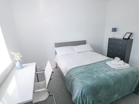 A bedroom with a bed covered by a green blanket a white desk and chair with flowers in a vase and a black dresser with a lamp and picture frame at Burry House in Llanmorlais